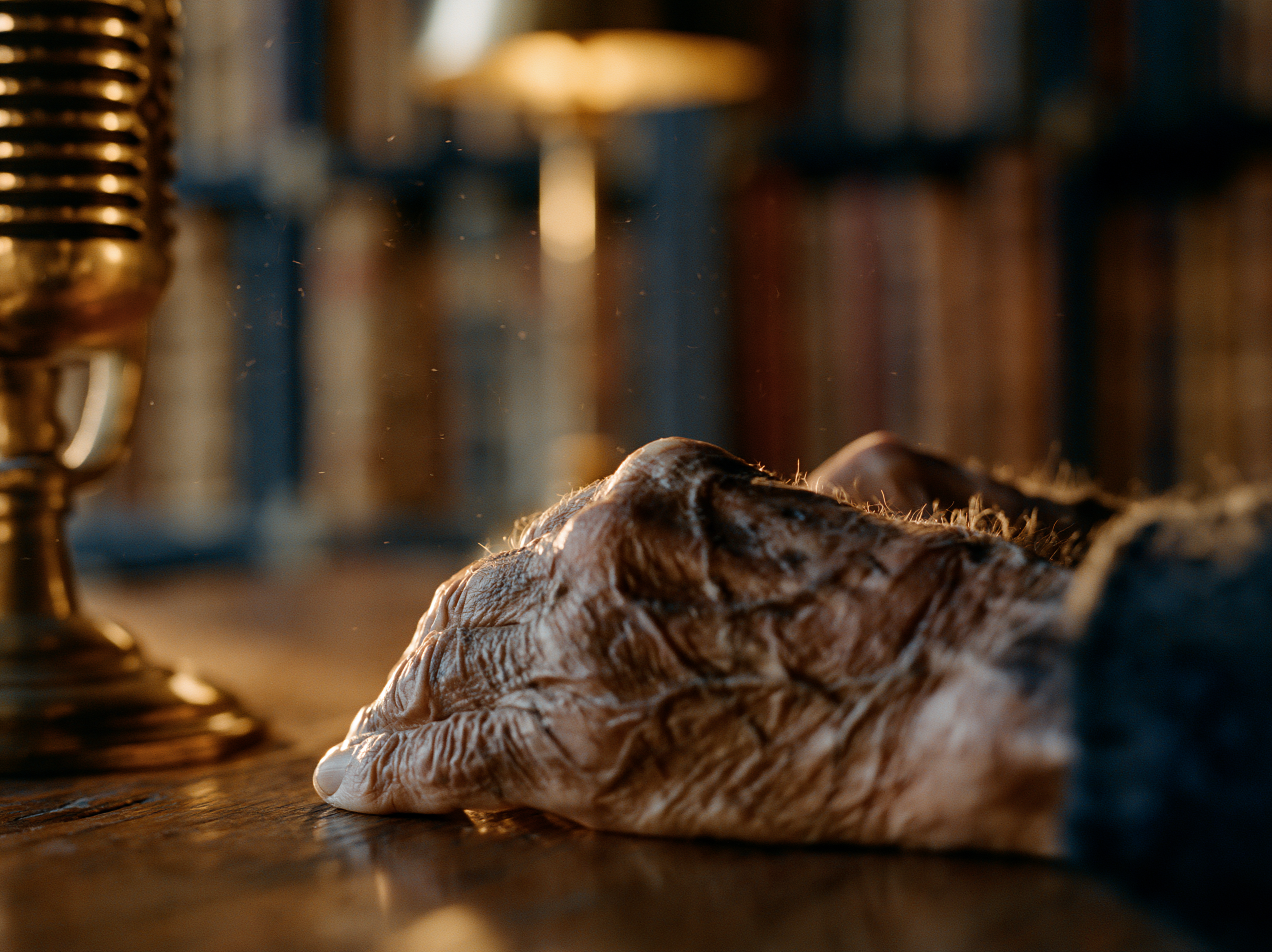 An elderly hand resting on a table beside a vintage brass microphone in warm lamplight